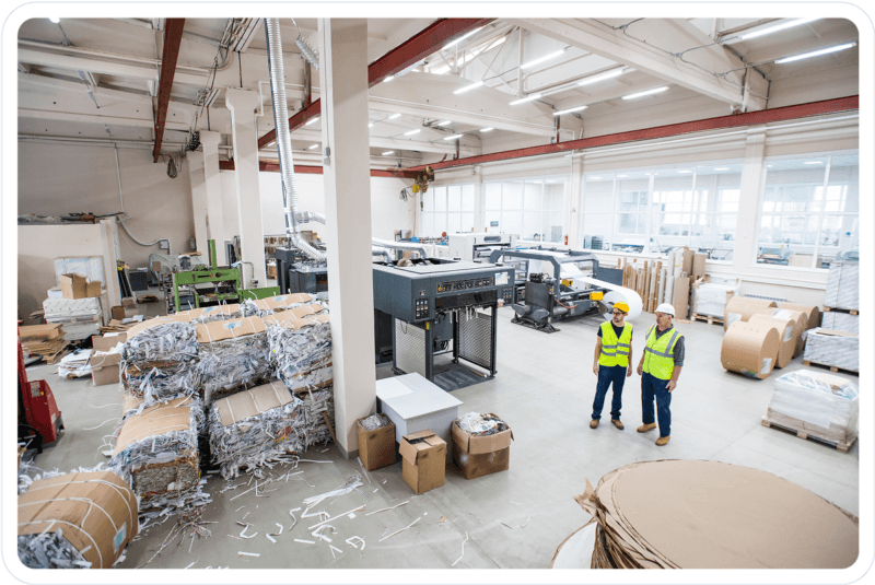 Engineers inspecting operations inside a pulp and paper manufacturing facility with machinery, shredded paper, and raw material rolls